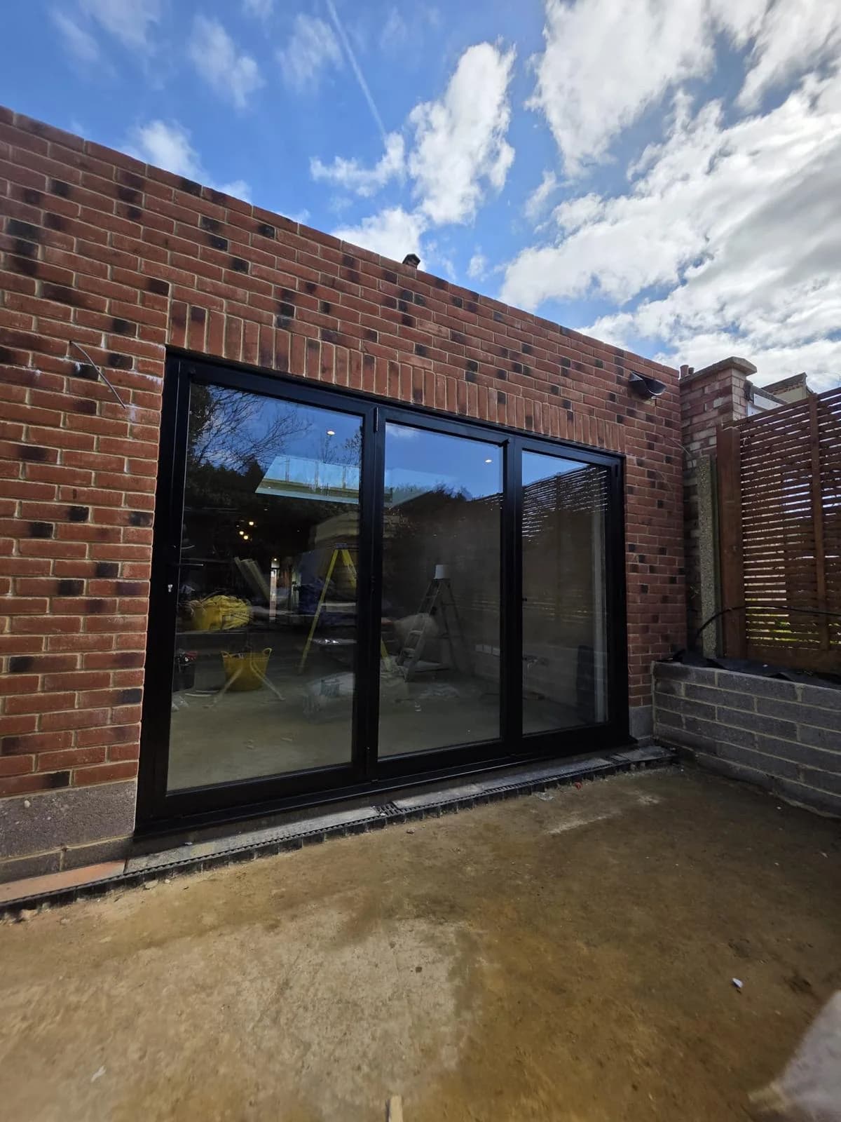 Black three-panel aluminium bi-fold doors installed by Cii Double Glazing in a brick extension, shown closed