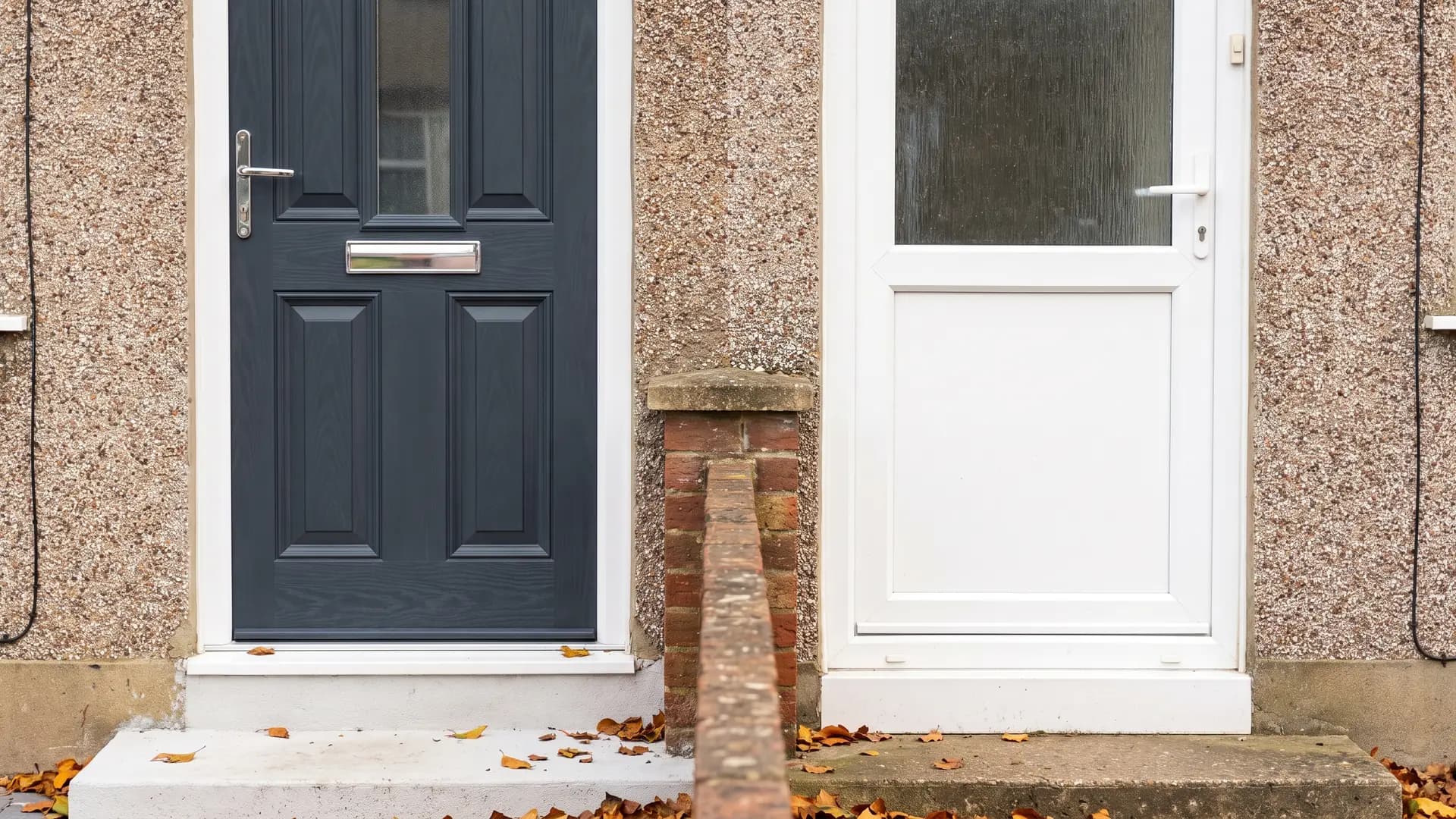 An anthracite grey composite front door beside a white half-glazed uPVC front door on a pair of pebble-dashed semi-detached houses