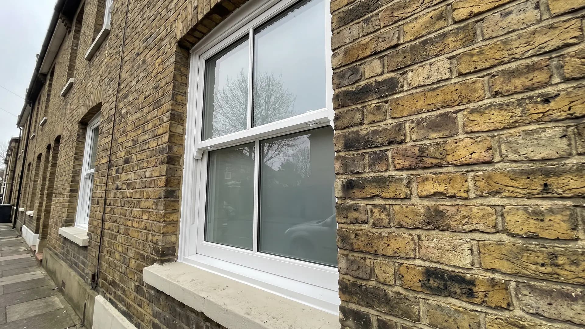 White double glazed sliding sash window with a two-over-two pane layout set back in the brick reveal of a yellow brick terraced house