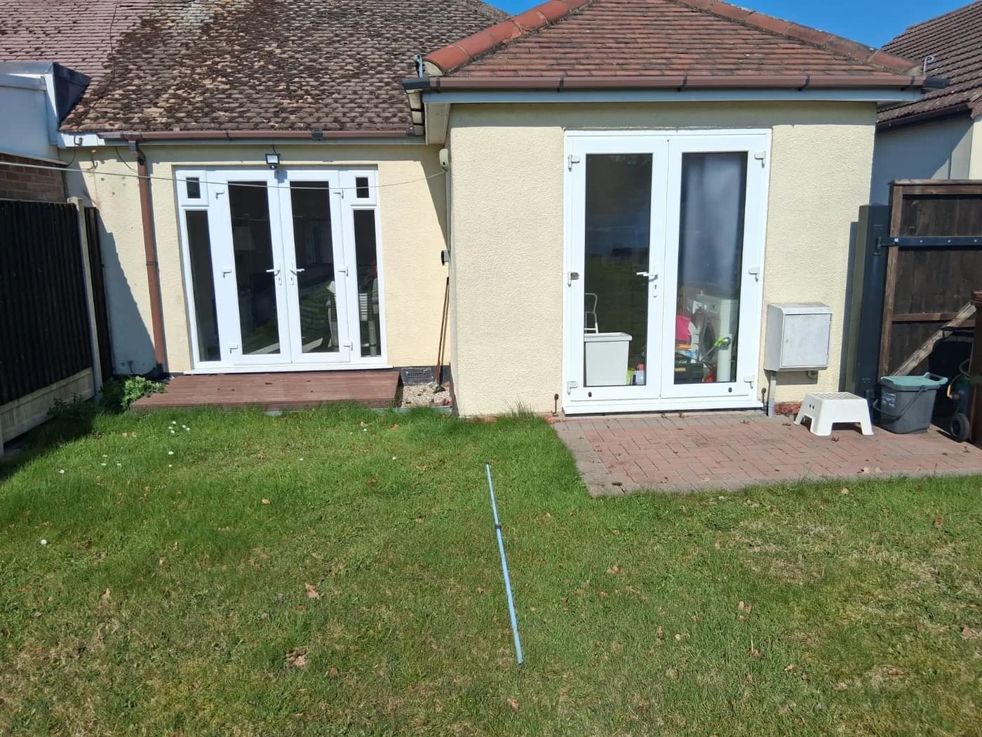 Two pairs of white uPVC French doors on the rear of a bungalow in Chelmsford, installed by Cii Double Glazing, opening onto decking and a brick patio