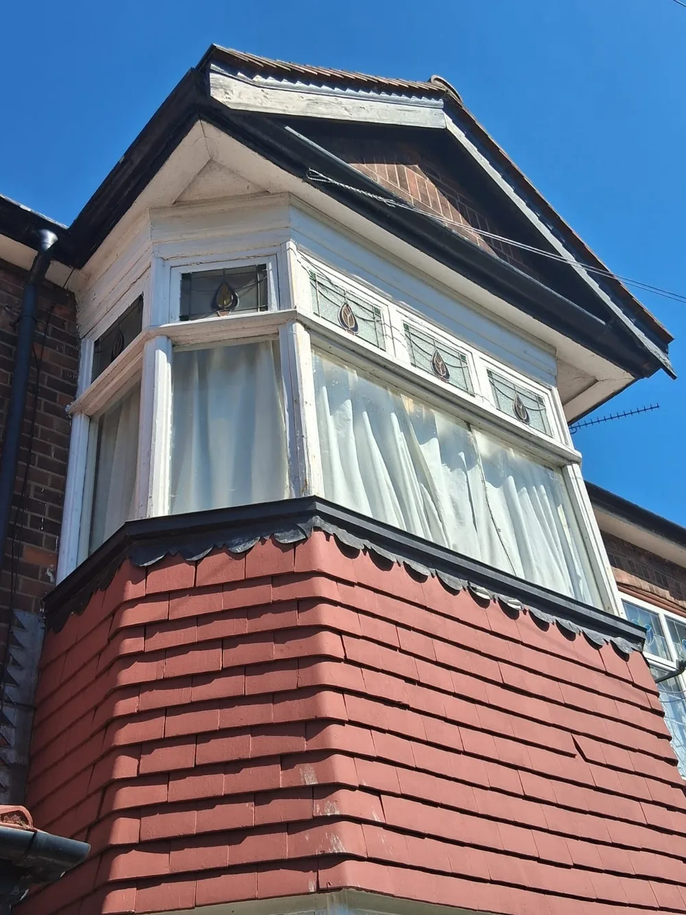 Older painted timber bay window with leaded top lights, its own pitched roof and a tile-hung base on a house in Chelmsford